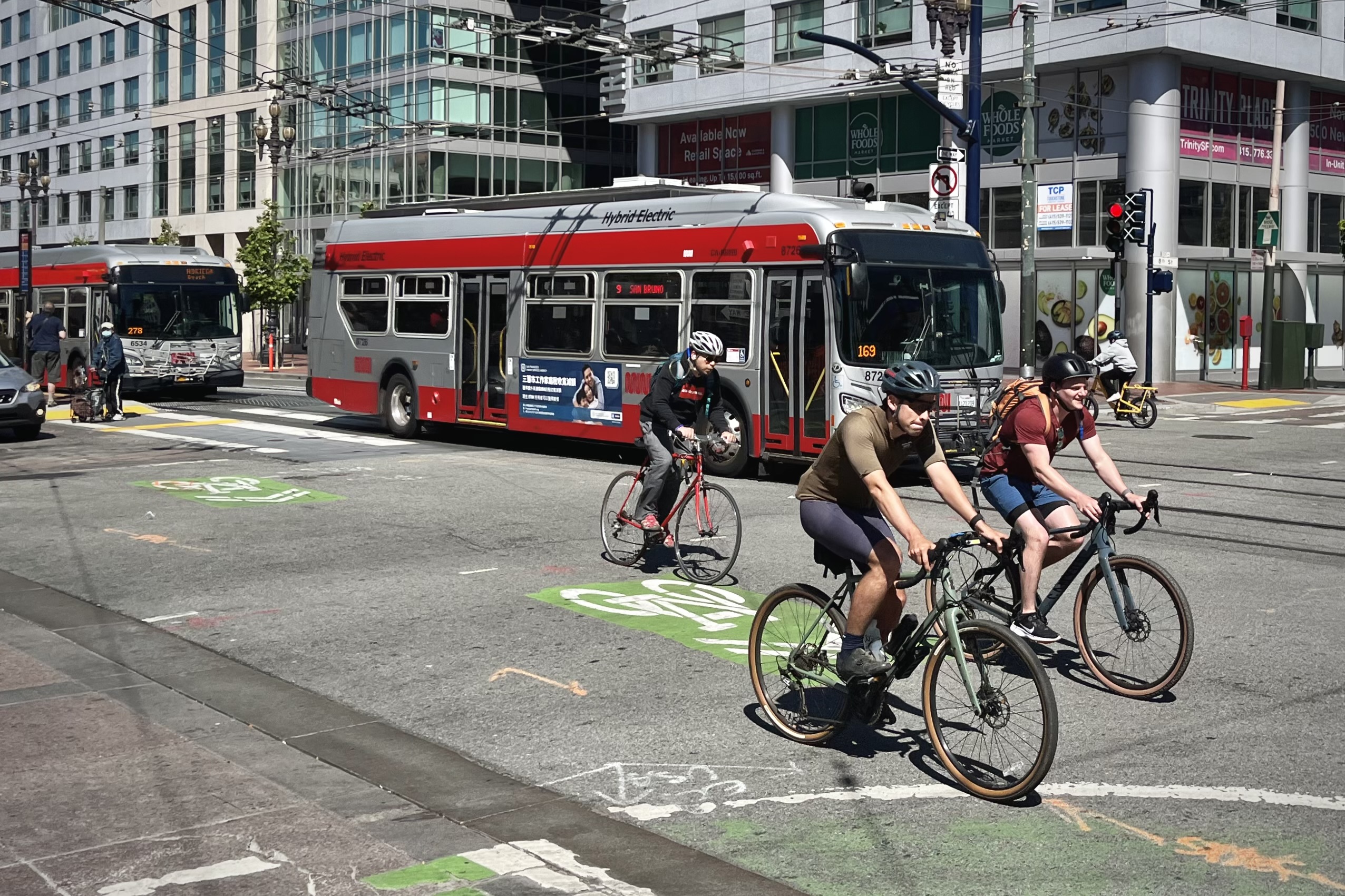 Cyclists riding alongside a pair of Muni buses on 8th Street.
